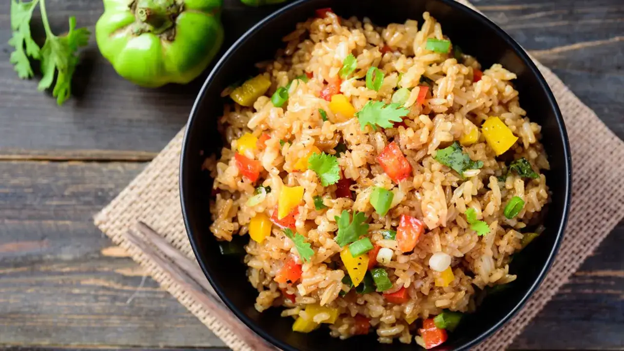 Un tazón de arroz con verduras salteadas, lleno de pimientos de colores y cilantro fresco, listo para disfrutar.