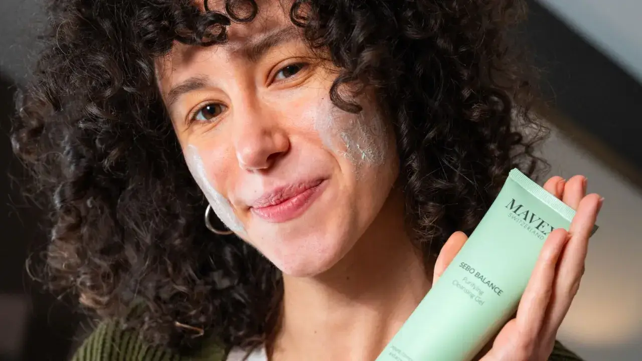 Donna con capelli ricci e maschera sul viso, tiene in mano un tubetto di 