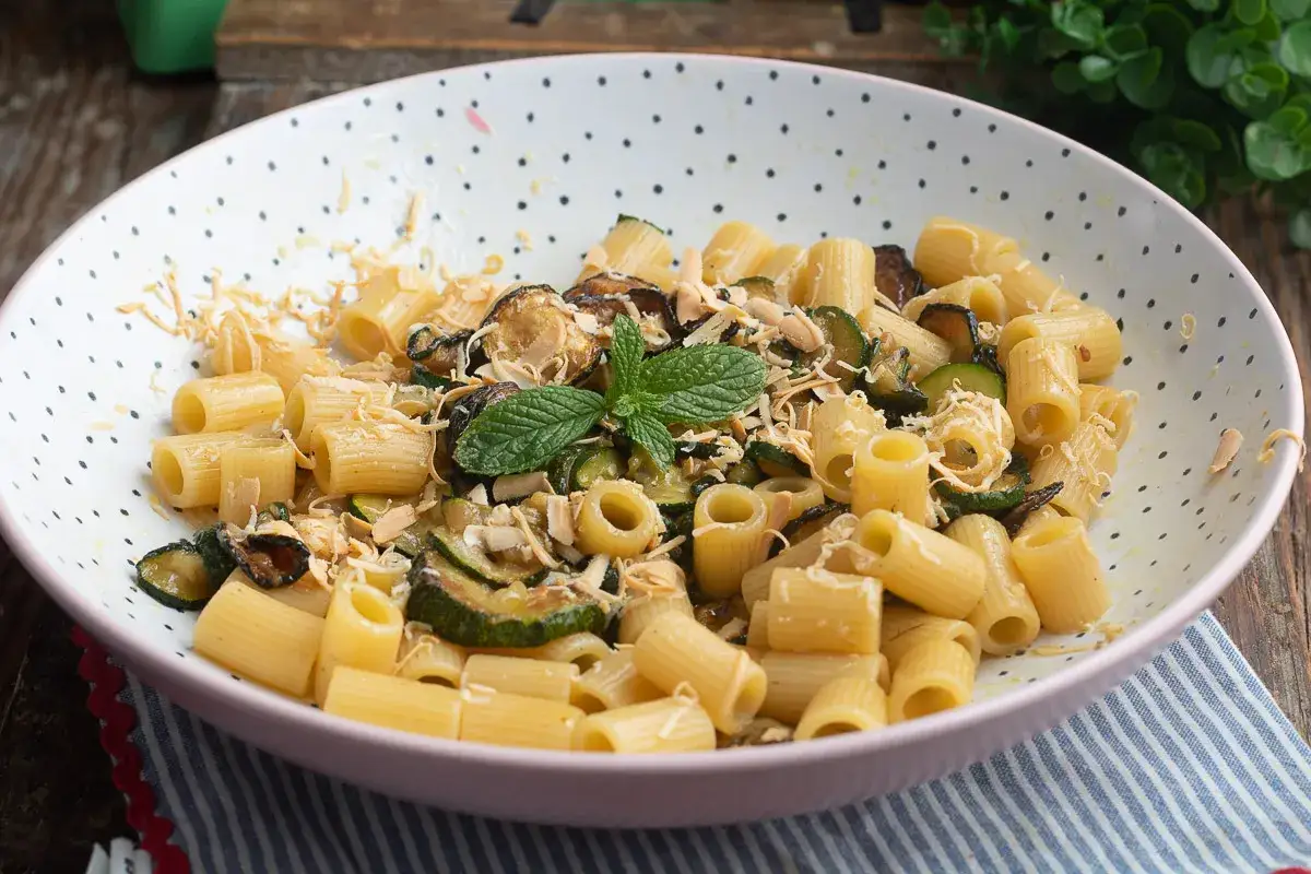 Piatto di pasta e zucchine alla siciliana, guarnito con menta fresca e scaglie di mandorle.