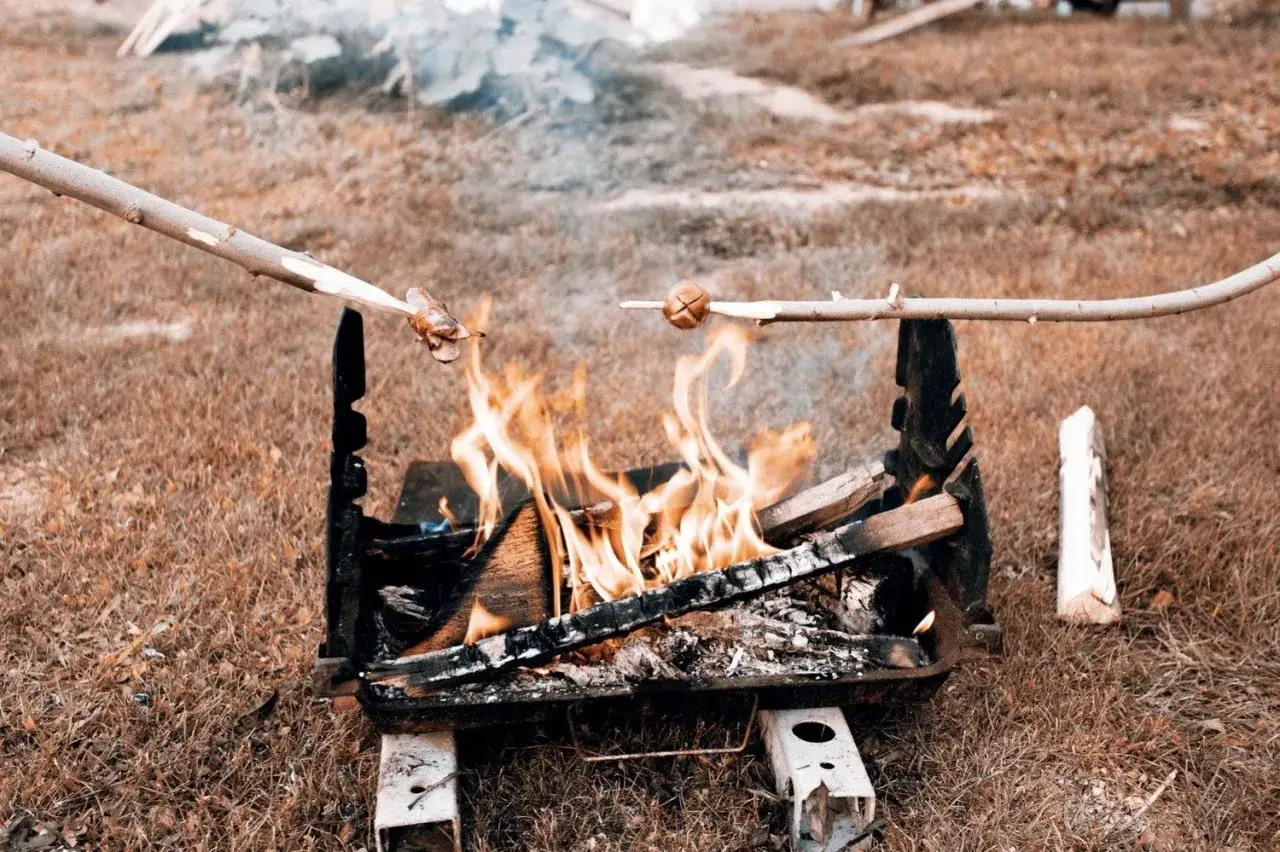 Kiełbasa na ognisko piecze się nad płomieniami. Dwie gałązki z kiełbaskami wiszą nad paleniskiem, tworząc idealną atmosferę do grillowania.