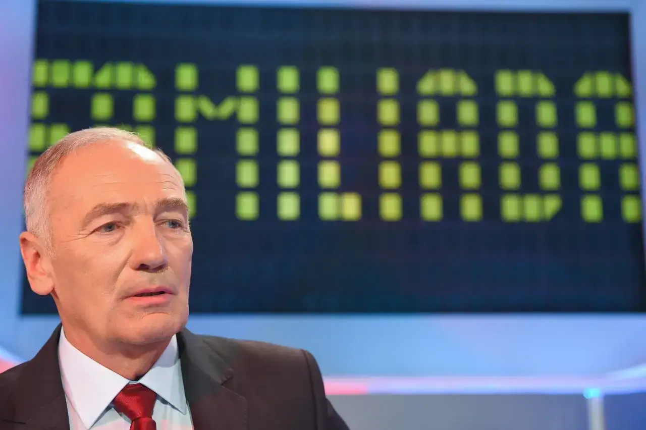 Mężczyzna w garniturze przed ekranem z zielonymi kwadratami. Czy rodzina pracowników TVP może brać udział w teleturnieju?