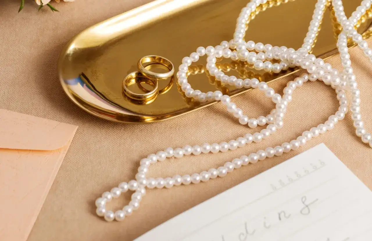 Złota tacka z obrączkami, naszyjnik z pereł i koperta. Co oznaczają perły w prezencie? Symbolizują czystość i elegancję.