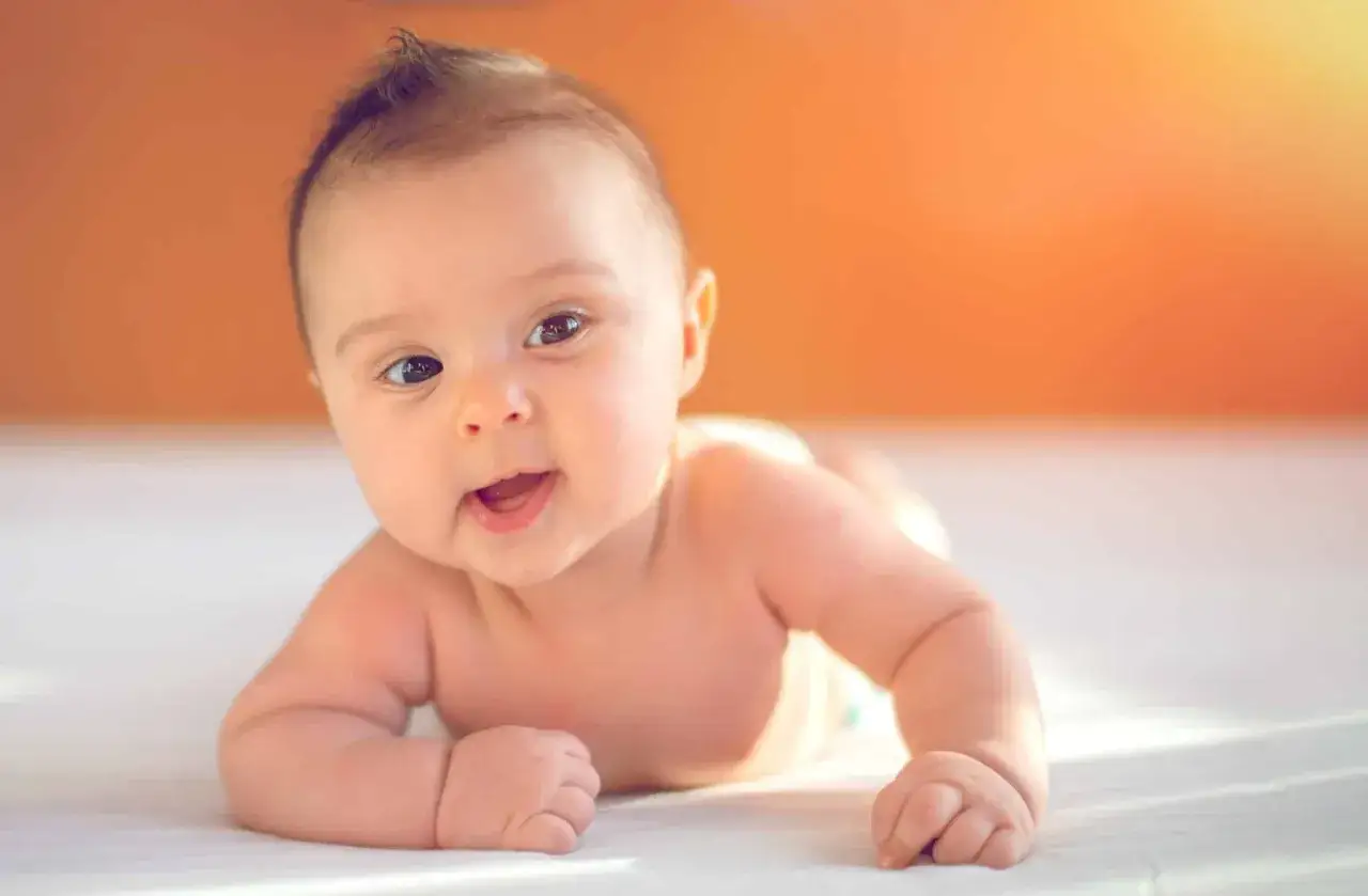 Ein Baby liegt auf dem Bauch, die Augen weit offen und lächelnd. Es ist ein typisches Bild für den 12 wochen schub, voller Entdeckungsfreude.