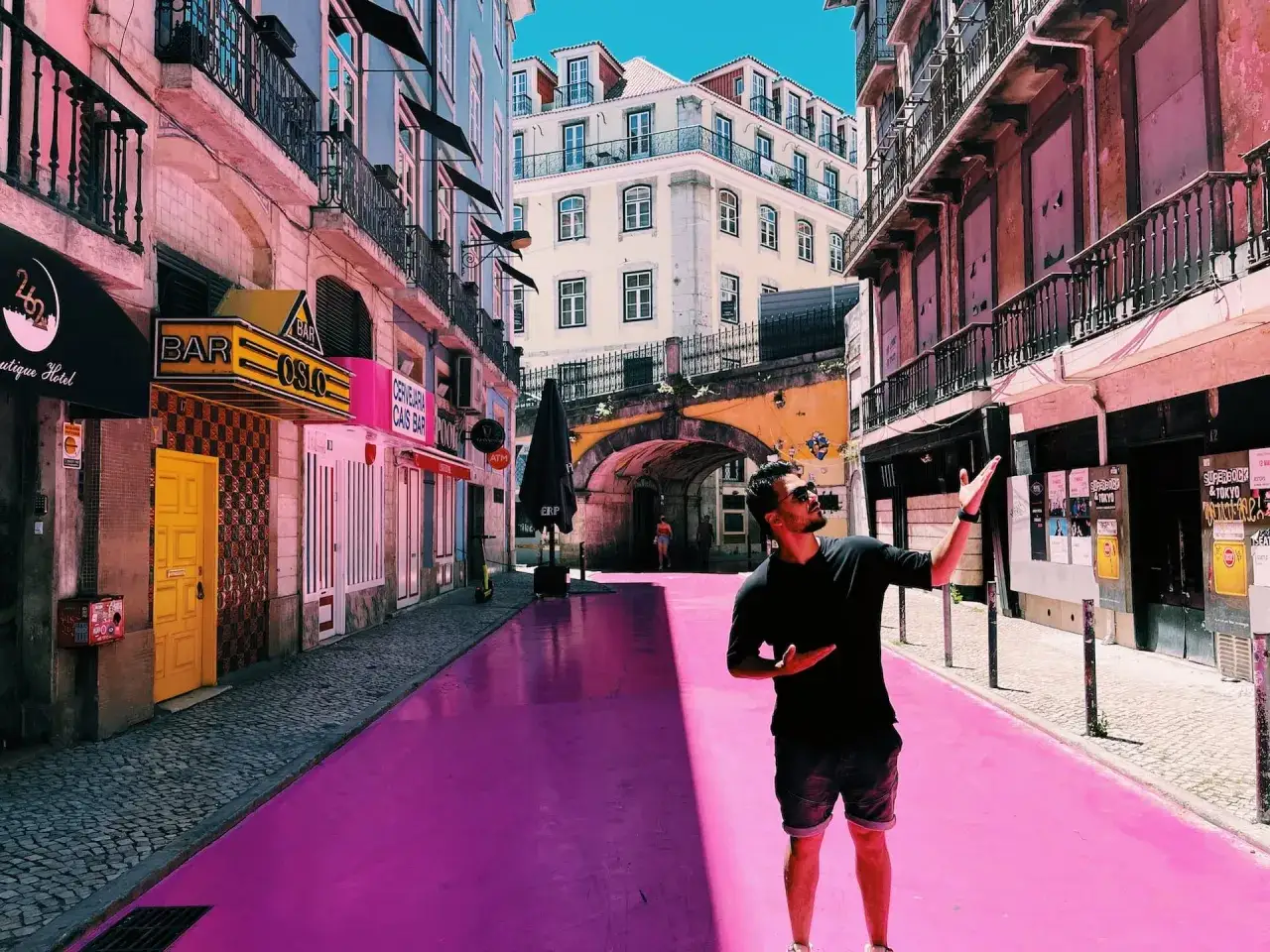 Mann steht auf pinker Straße in Lissabon, vorbei an Bars wie