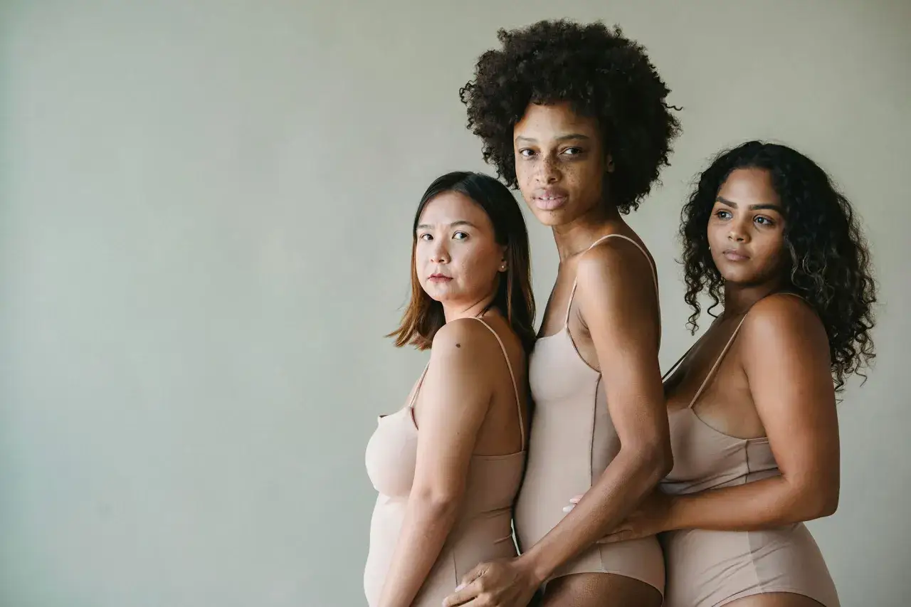 Tre donne di diverse etnie, in body color carne, mostrano la loro bellezza naturale. La frase 