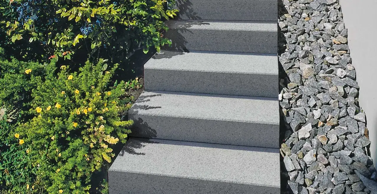 Escalier extérieur en béton gris, avec une végétation luxuriante et des pierres décoratives. La profondeur marche escalier extérieur est bien visible.