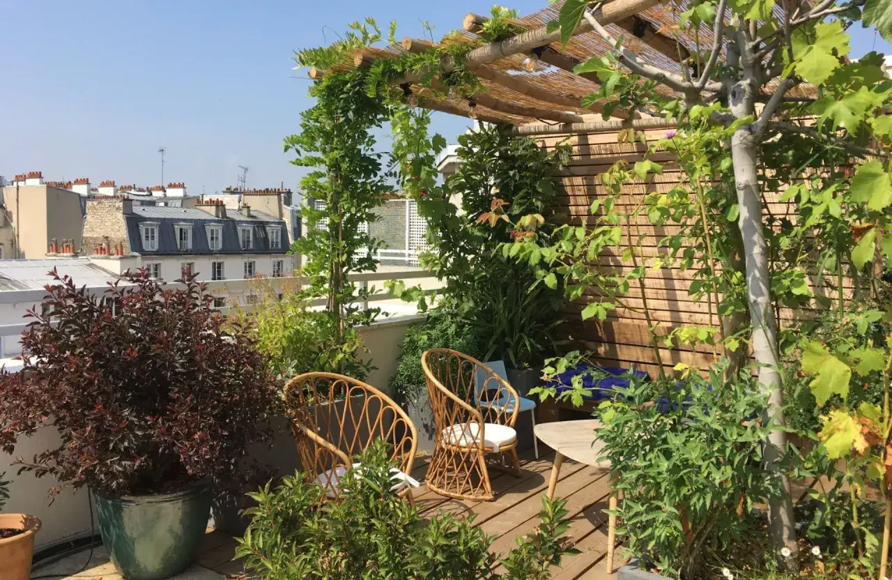 Aménagement toit terrasse verdoyant avec chaises en rotin et pergola en bois. Vue sur les toits de Paris.