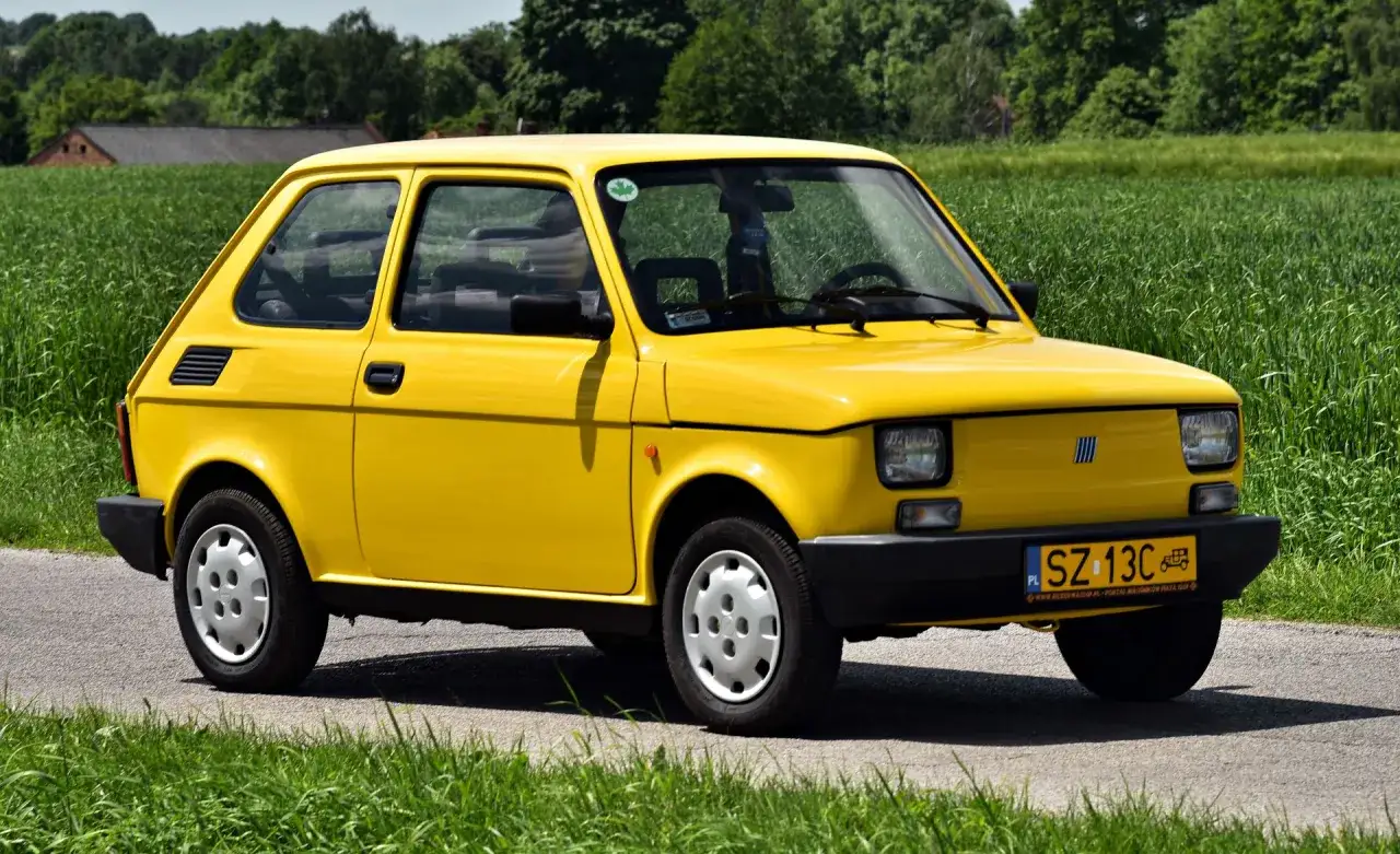 Żółty Fiat 126p na tle zielonego pola. Zastanawiasz się, czy warto zarejestrować auto jako zabytek?