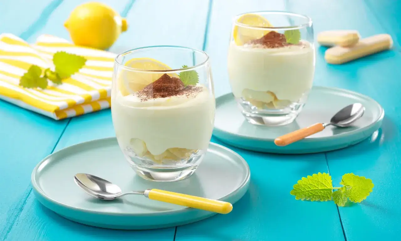 Zwei Gläser mit cremigem Zitronen Tiramisu, garniert mit Kakaopulver und Zitronenscheiben. Ein erfrischender Genuss!