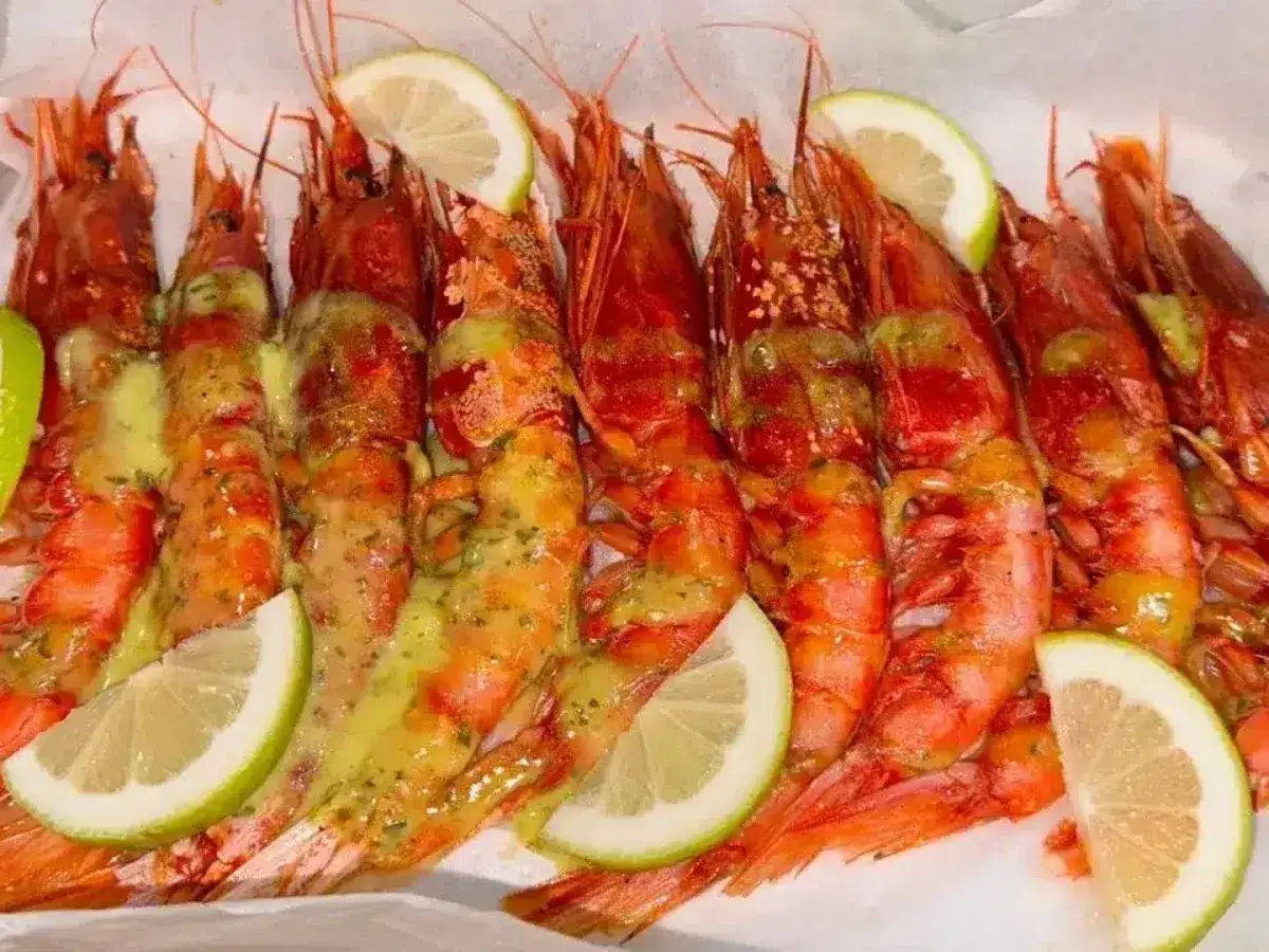 Gamberoni al forno succulenti, conditi con una salsa dorata e guarniti con spicchi di limone fresco.