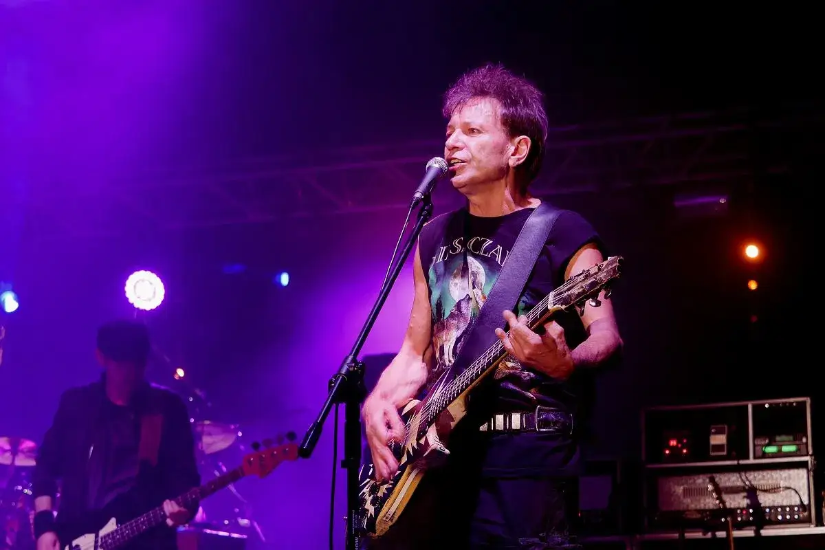 Wokalista zespołu KSU gra na gitarze i śpiewa do mikrofonu. Na scenie panuje fioletowe oświetlenie.