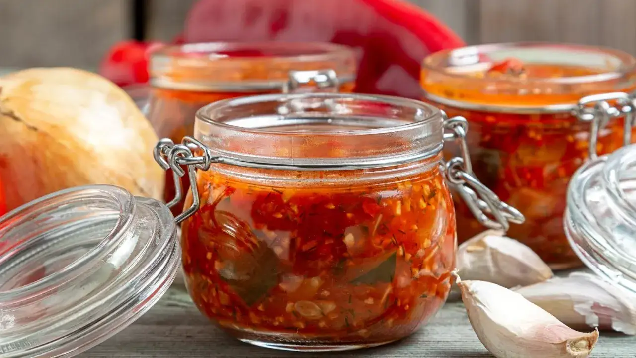 Domowy sos sriracha z papryczek chilli i czosnku w słoikach, obok cebuli i czosnku.