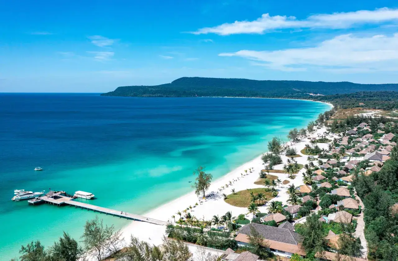 Traumhafter kambodscha strand mit t&uuml;rkisfarbenem Wasser, wei&szlig;em Sand, einem Steg mit Booten und tropischen Bungalows.