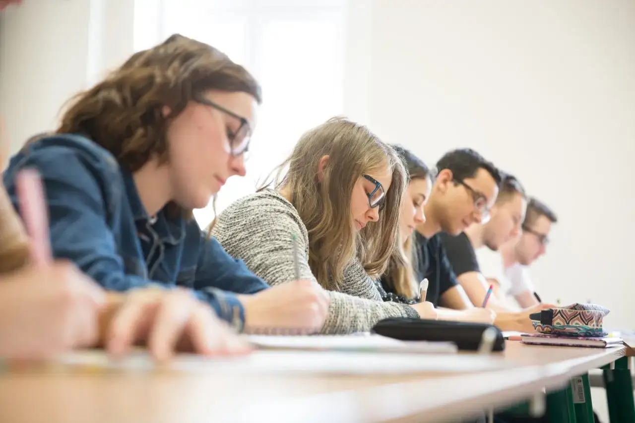 Studenci filologii słowiańskiej pochyleni nad zeszytami, skupieni na zajęciach.