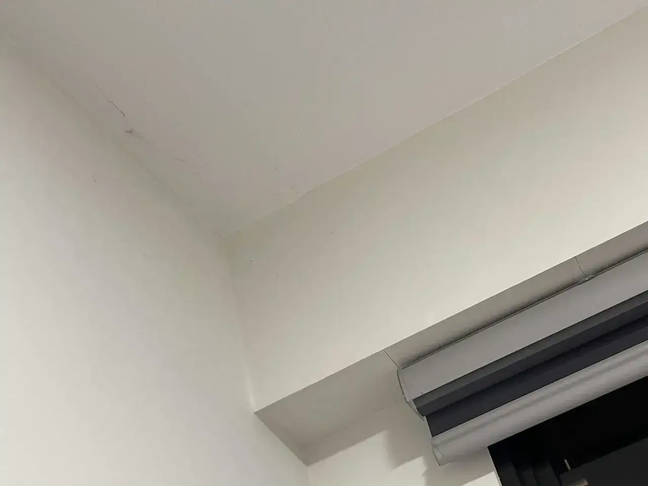 Angolo di un muro bianco con un piccolo nido di ragno e fili sottili.