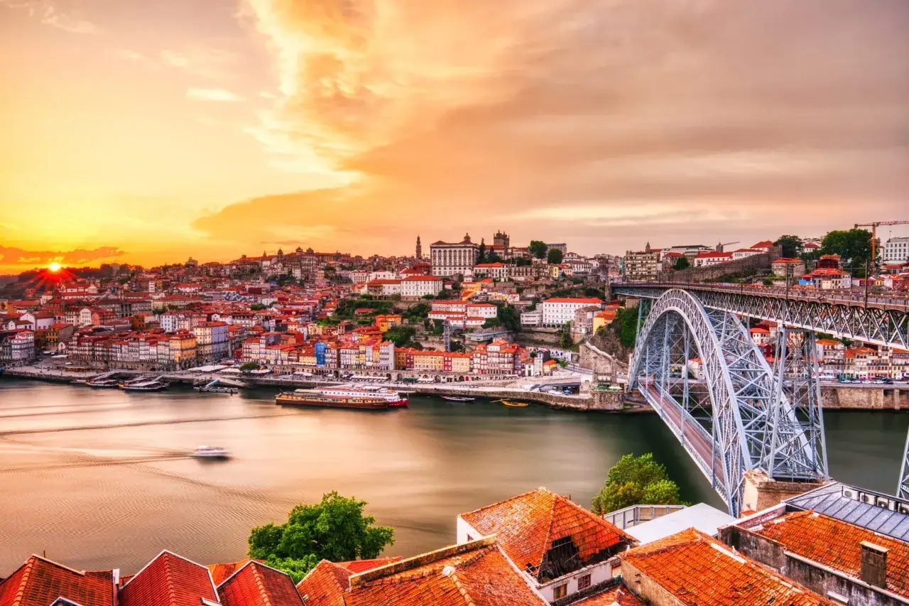 Sonnenuntergang über Porto mit der Dom Luís I Brücke und dem Fluss Douro. Die bunten Häuser der Stadt leuchten im warmen Licht.