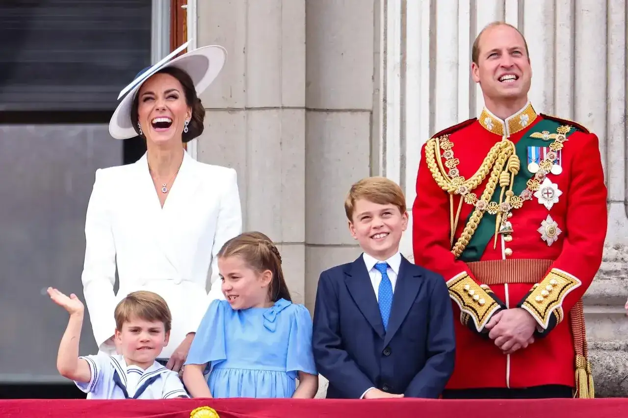 William i Kate z dziećmi na balkonie. Książę Louis macha, Charlotte i George uśmiechnięci.