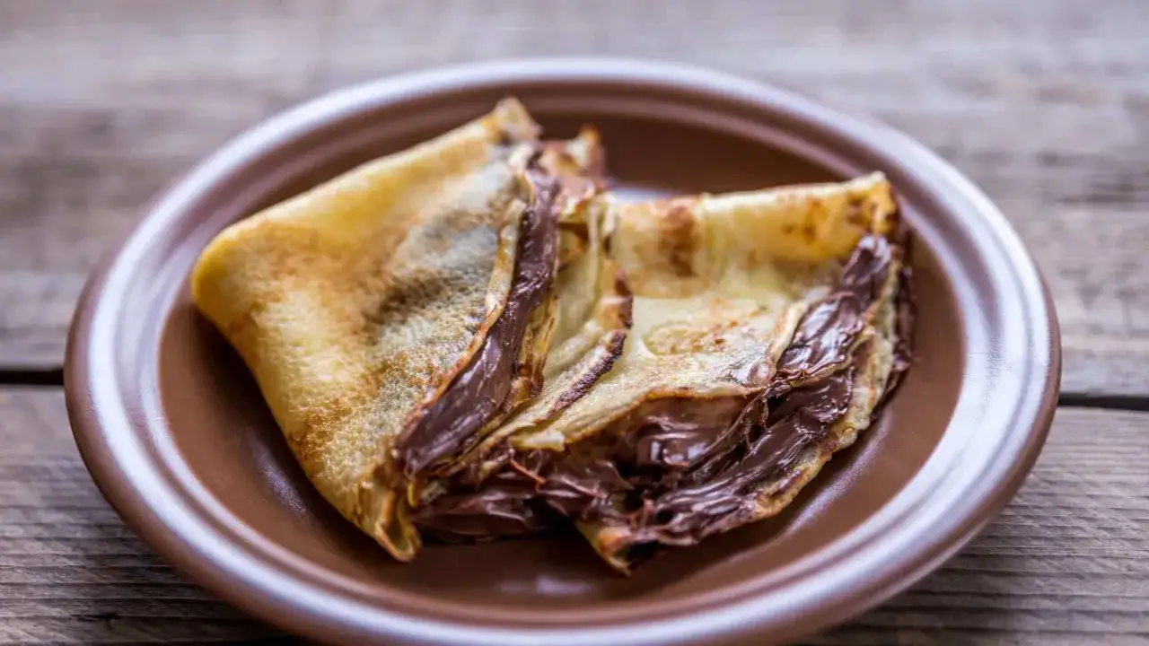 Crêpes garnies de nutella liquide pour crêpe, sur une assiette marron.