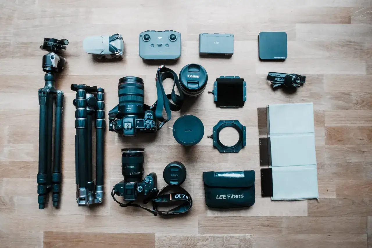 Zestaw sprzętu fotograficznego: dwa statywy, drony, kontrolery, aparaty Canon i Sony, obiektywy, uchwyt na filtry, lampka czołowa i filtry do zdjęć LEE Filters.
