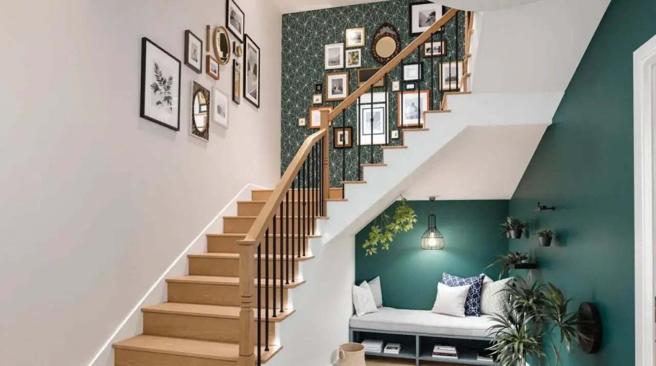 Une galerie de cadres décore le mur de la cage d'escalier. Une banquette confortable et des plantes vertes complètent cette idée déco cage escalier.