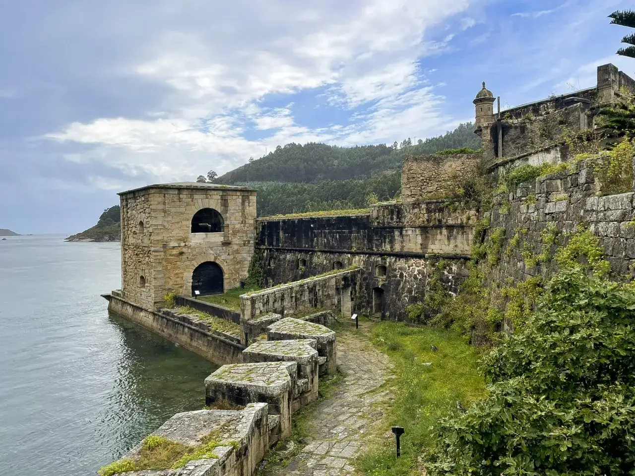Antiguo castillo de la Palma, con sus muros de piedra y vegetación, junto al mar.