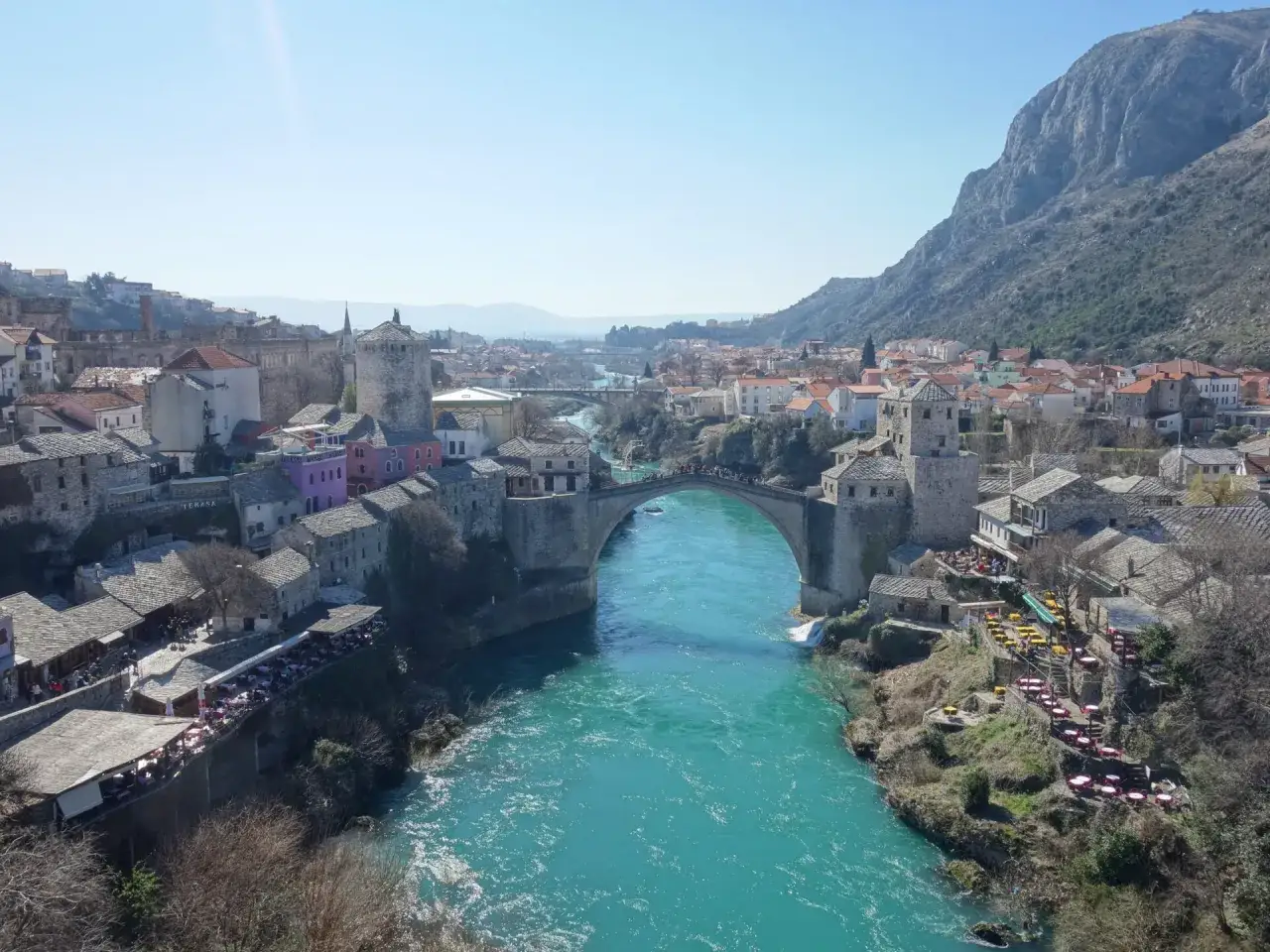 Mostar, Bośnia i Hercegowina: słynny Stary Most nad turkusową rzeką Neretwą, otoczony kamiennymi budynkami i g&oacute;rami.