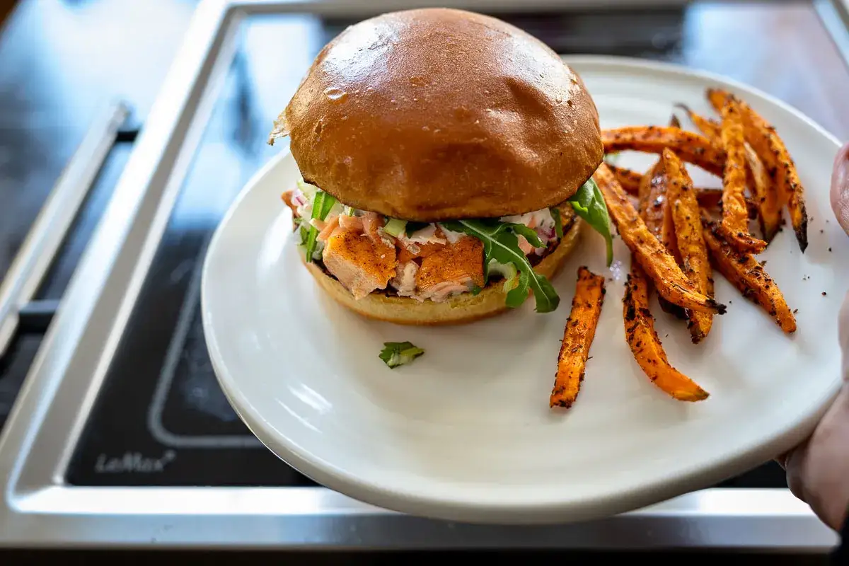 Saftiger Burger mit pulled Lachs, knackigem Salat und knusprigen Süßkartoffel-Pommes auf einem Teller.