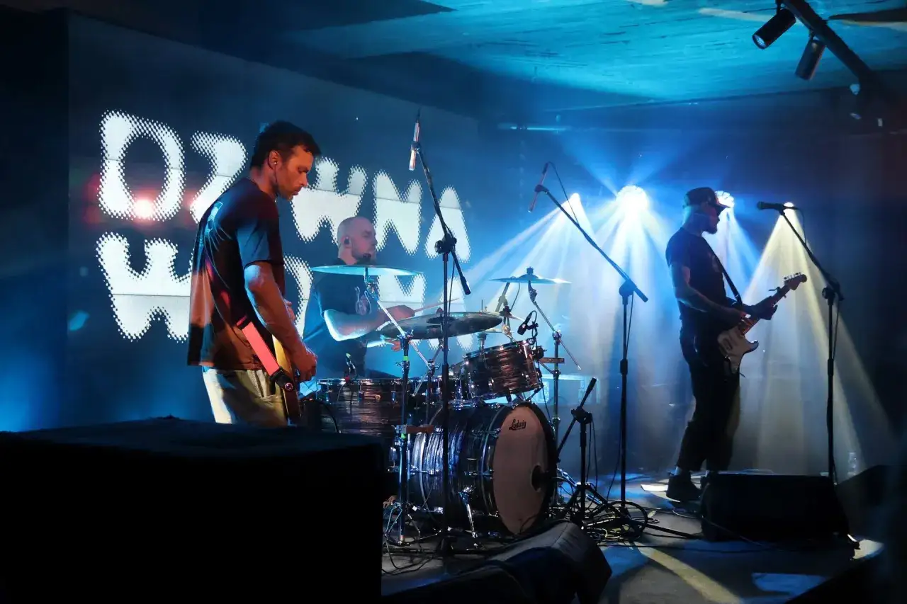 Koncert zespołu Dziwna Wiosna. Gitarzysta i perkusista na scenie, w tle logo zespołu.