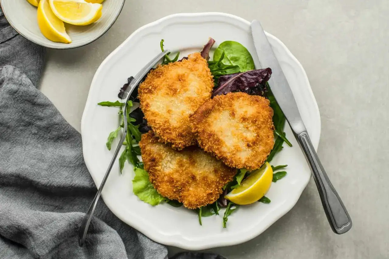 Trois escalopes milanaises dorées et croustillantes, servies sur un lit de salade verte avec des quartiers de citron.
