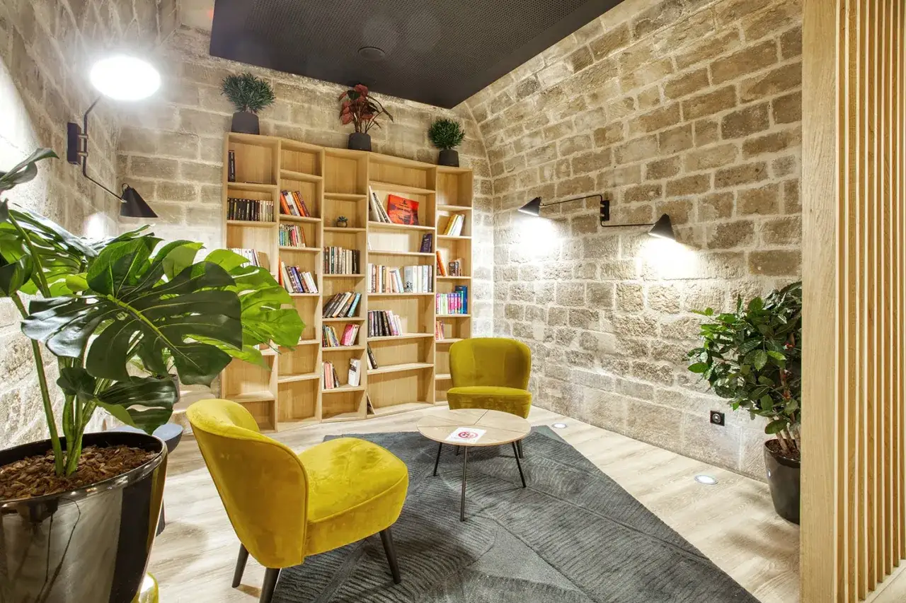 Un coin salon cosy avec deux fauteuils moutarde, une bibliothèque remplie de livres et des plantes vertes. Un espace de vie invitant à la détente.