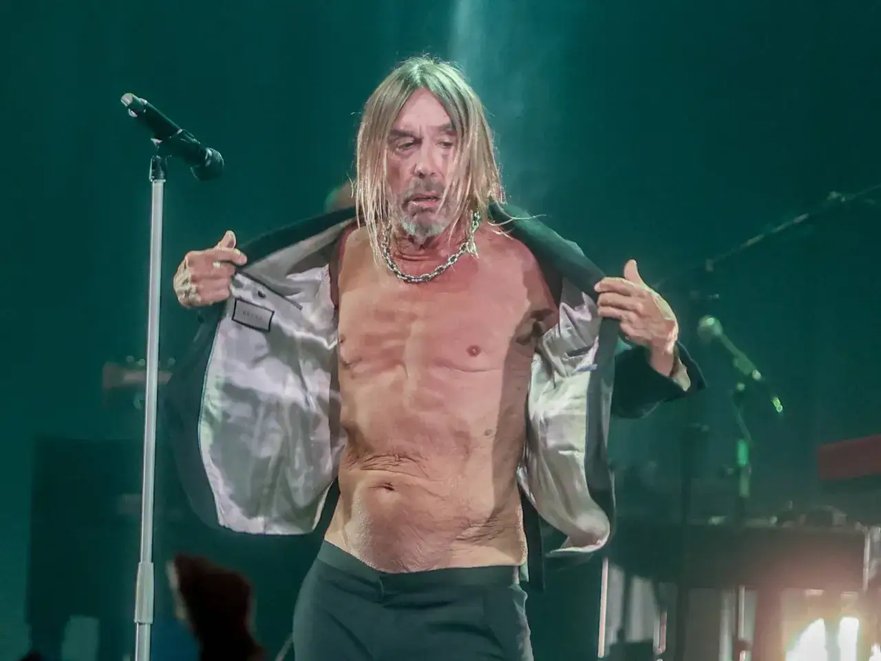 Iggy Pop na scenie, zdejmuje marynarkę, odsłaniając tors. W tle Kacperczyk.