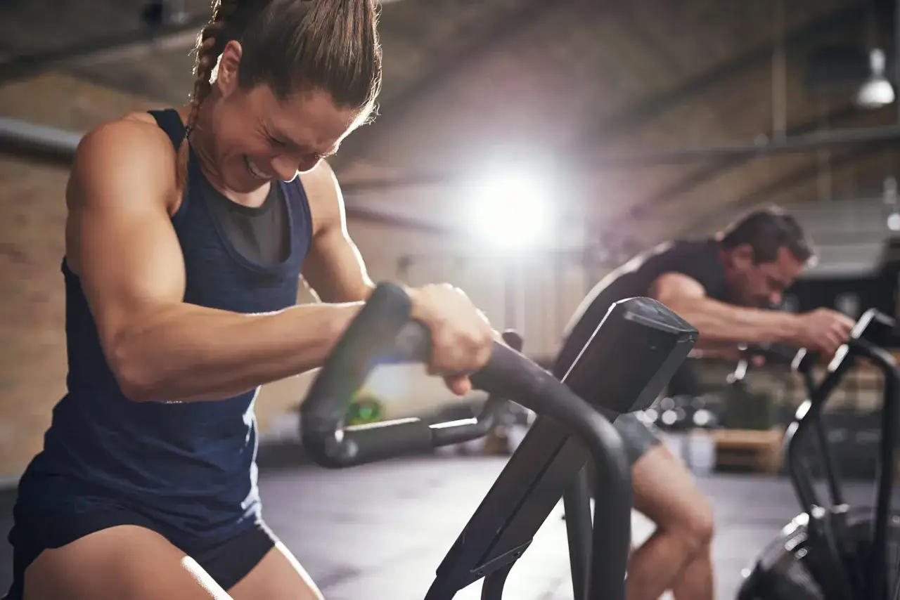 A woman strains on a stationary bike, her face contorted in effort. This intense workout shows how a stationary bike can help with running by building endurance.