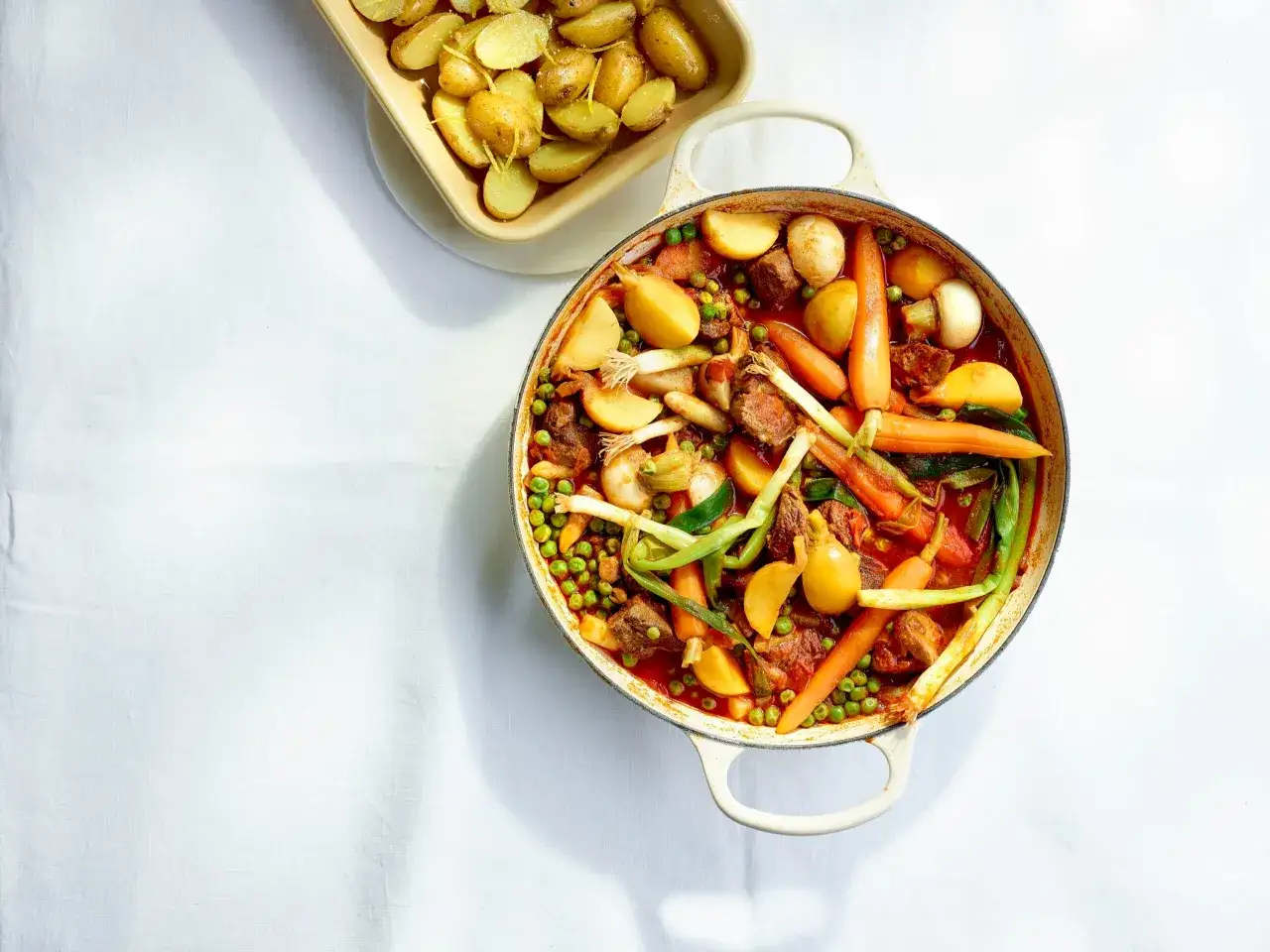 Un plat mijoté de ragout d'agneau avec des carottes, des pommes de terre, des petits pois et des oignons verts, servi dans une cocotte.