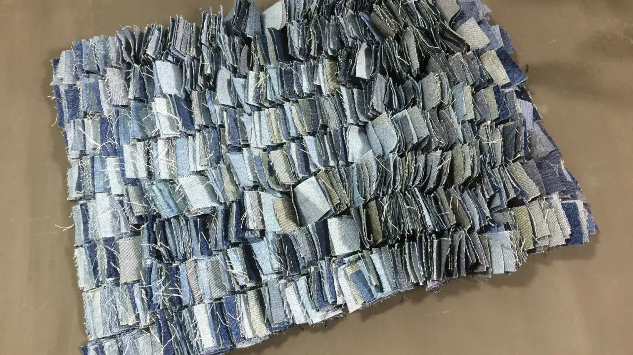 Detaljerad vy av en matta som h&aring;ller p&aring; att sy ihop trasmattor av jeans.