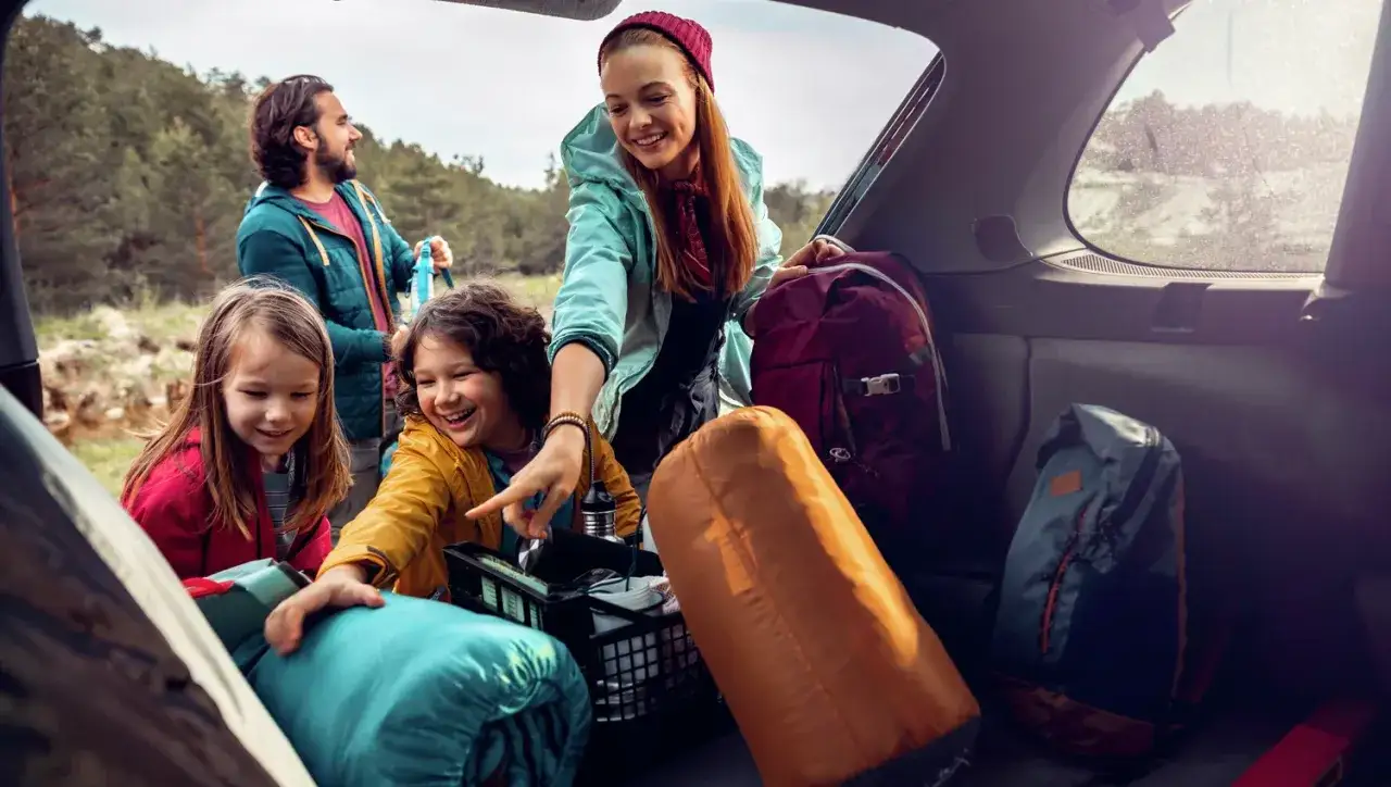 Familjen packar bilen för en härlig semester. Barnen hjälper till att lägga ner sovsäckar och ryggsäckar, en perfekt packlista semester!