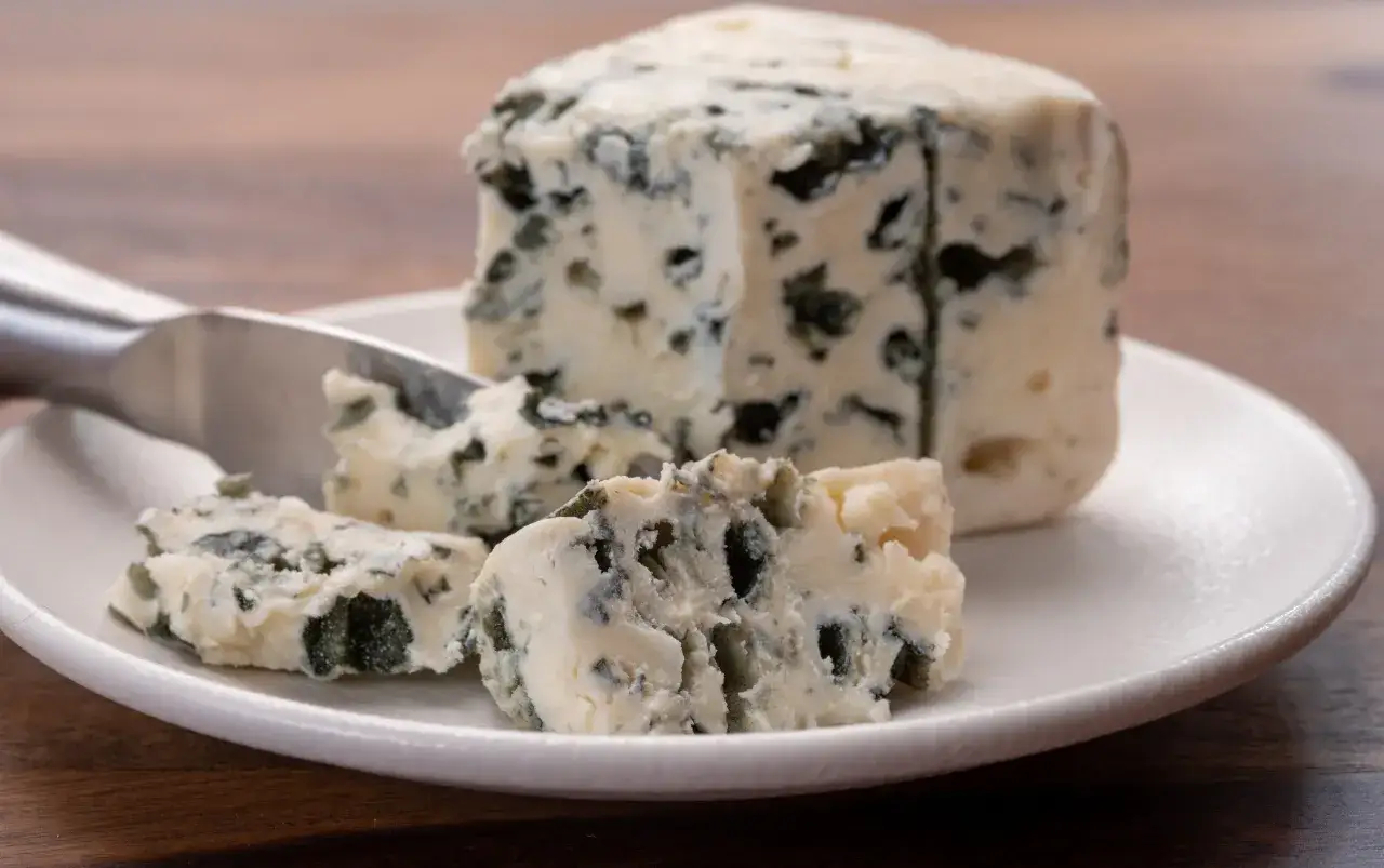 Un pezzo di formaggio con muffa nome, con venature blu intenso, su un piatto bianco. Un coltello da formaggio è appoggiato accanto.