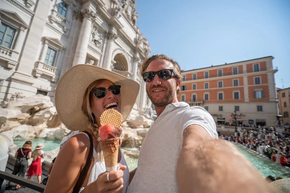 Para, delektując się lodami, robi sobie selfie na tle Fontanny di Trevi. Idealne miasto na weekend we dwoje.