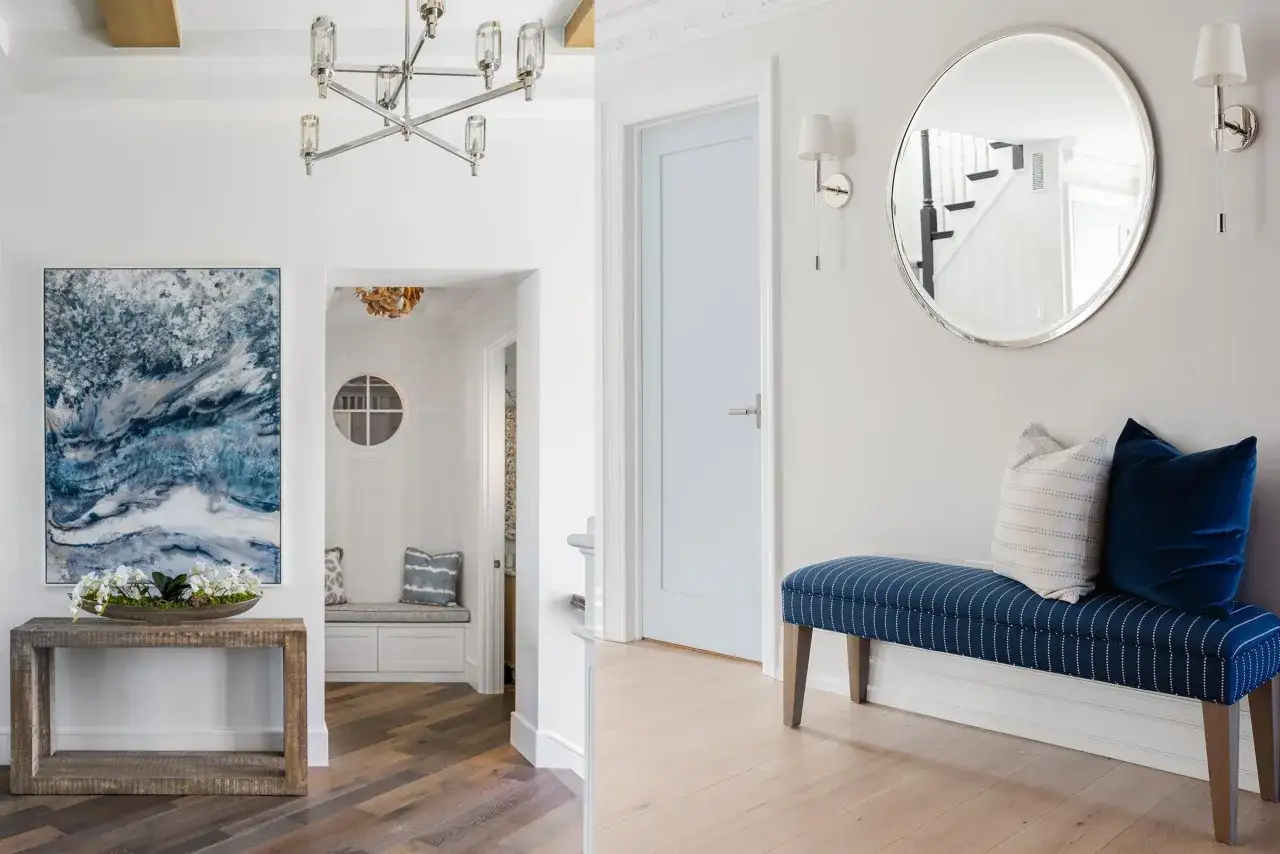 A modern entryway design featuring a rustic console table with abstract art, a built-in bench, and a striped bench with pillows, all under a stylish chandelier.