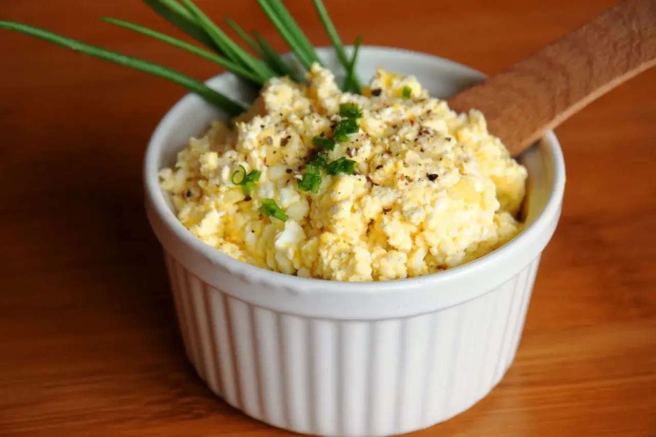 Pyszna pasta jajeczna z twarogiem, posypana szczypiorkiem i pieprzem, w białej miseczce. Idealna na śniadanie.