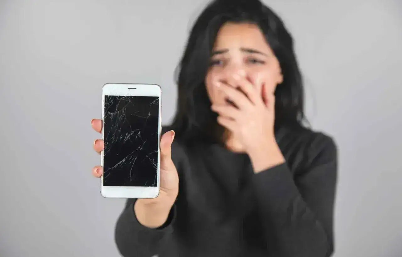 Zrozpaczona kobieta pokazuje telefon z pękniętym, ciemny ekranem.