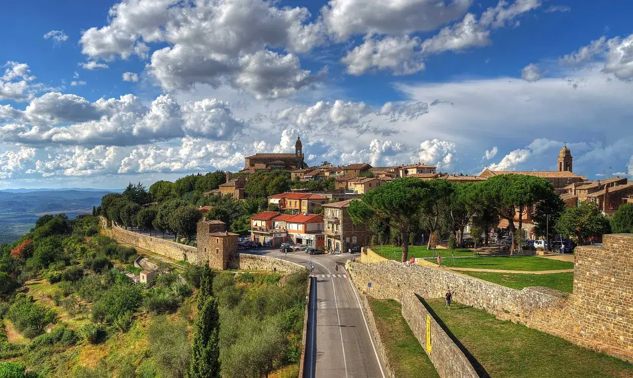 Un panorama mozzafiato per chi decide di visitare Montalcino: un borgo medievale su una collina, con case in pietra e torri, circondato da verde.