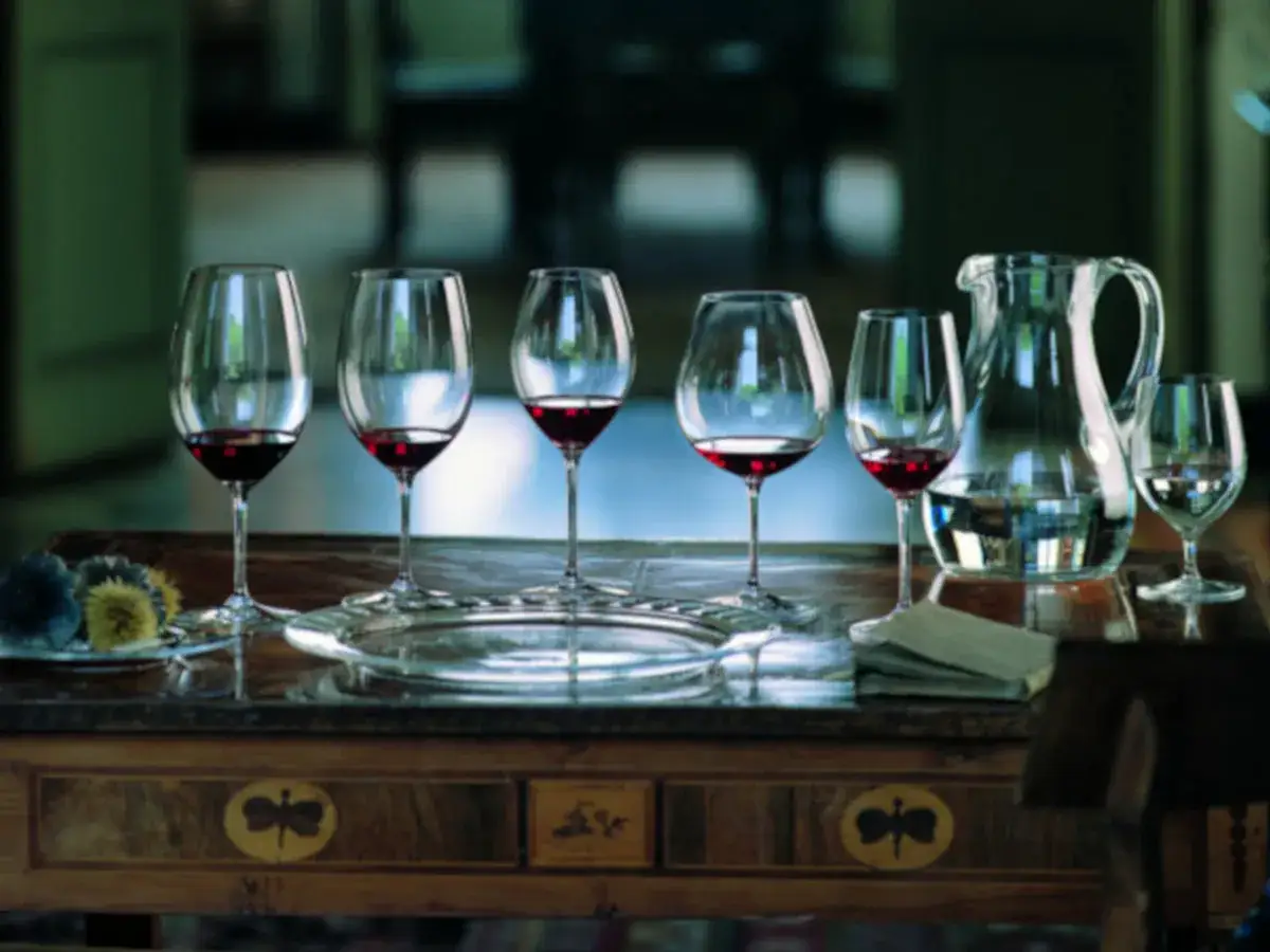Sechs Gl&auml;ser mit Rotwein, bereit f&uuml;r eine Verkostung von Cabernet Sauvignon vs. Merlot. Ein Krug mit Wasser und ein paar Dekorationen stehen daneben.
