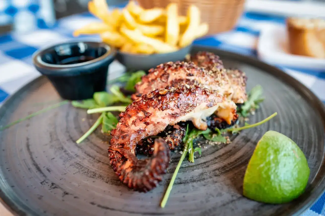 Tentacules de poulpe grillés, savamment préparés avec une marinade pour poulpe grillé, accompagnés de frites et d'une touche de citron vert.