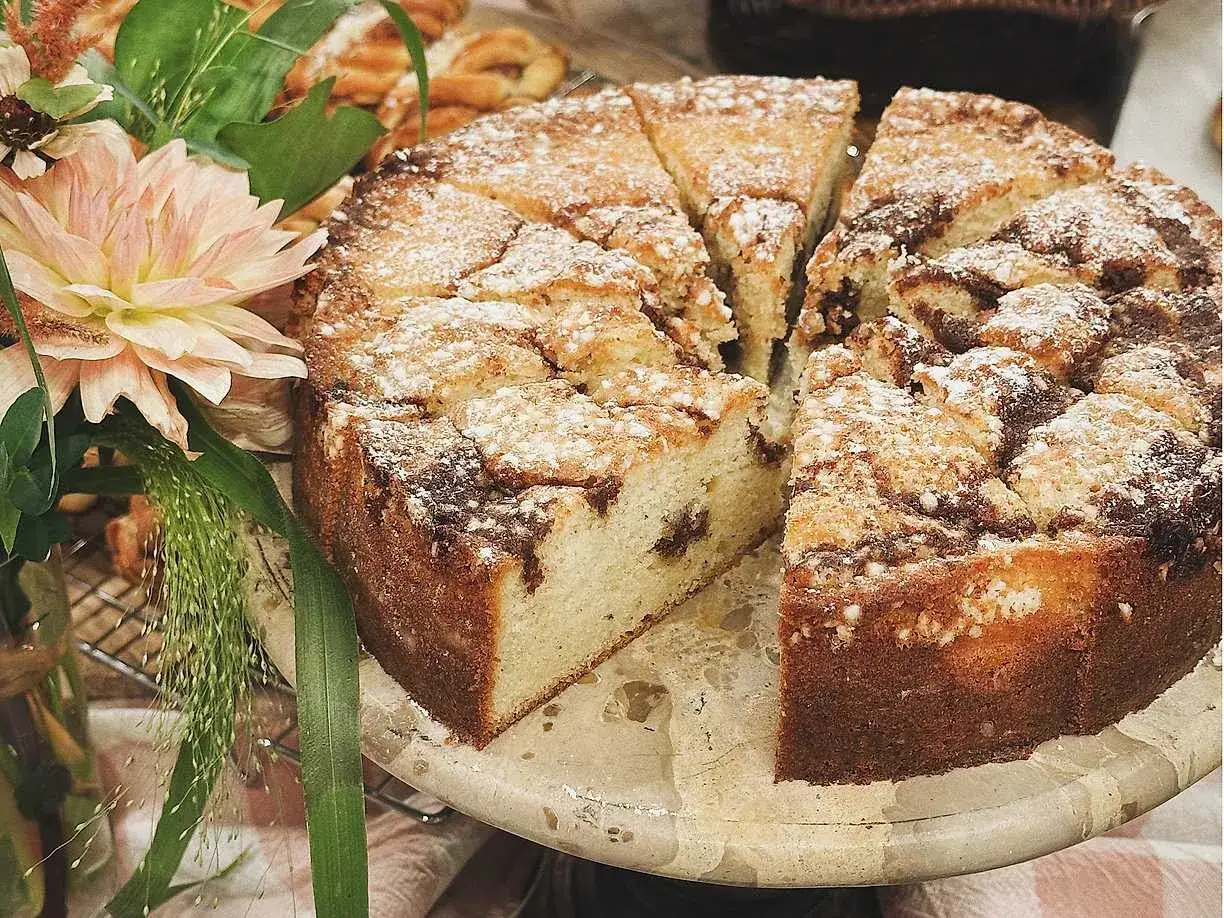 En saftig kanelbulle kaka, pudrad med florsocker, skuren i bitar. Bredvid står en vacker bukett blommor.