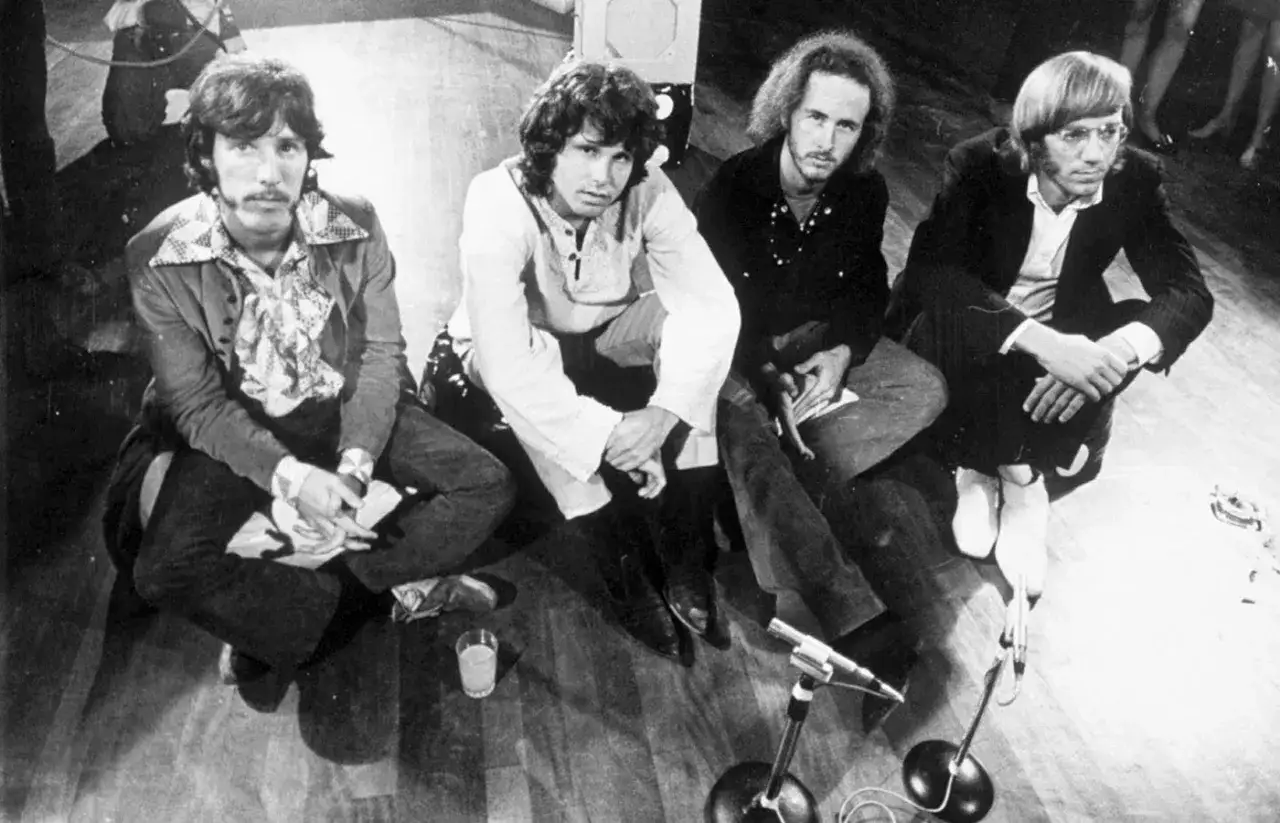 Czterech członk&oacute;w zespołu The Doors siedzi na podłodze, gotowych do występu.