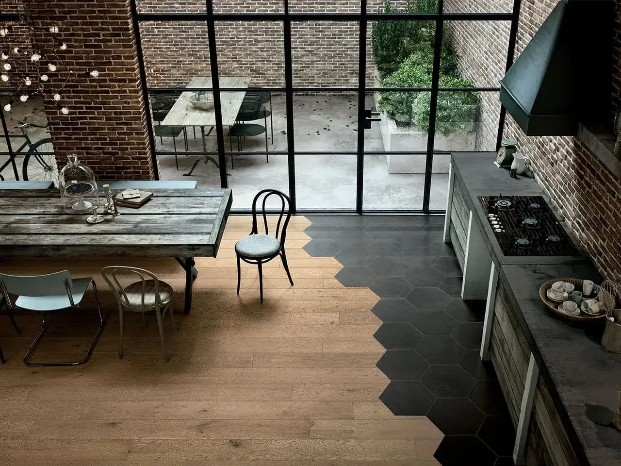 Un elegante accostamento parquet e piastrelle esagonali nere crea un design moderno in questa cucina con mattoni a vista e un grande tavolo in legno.
