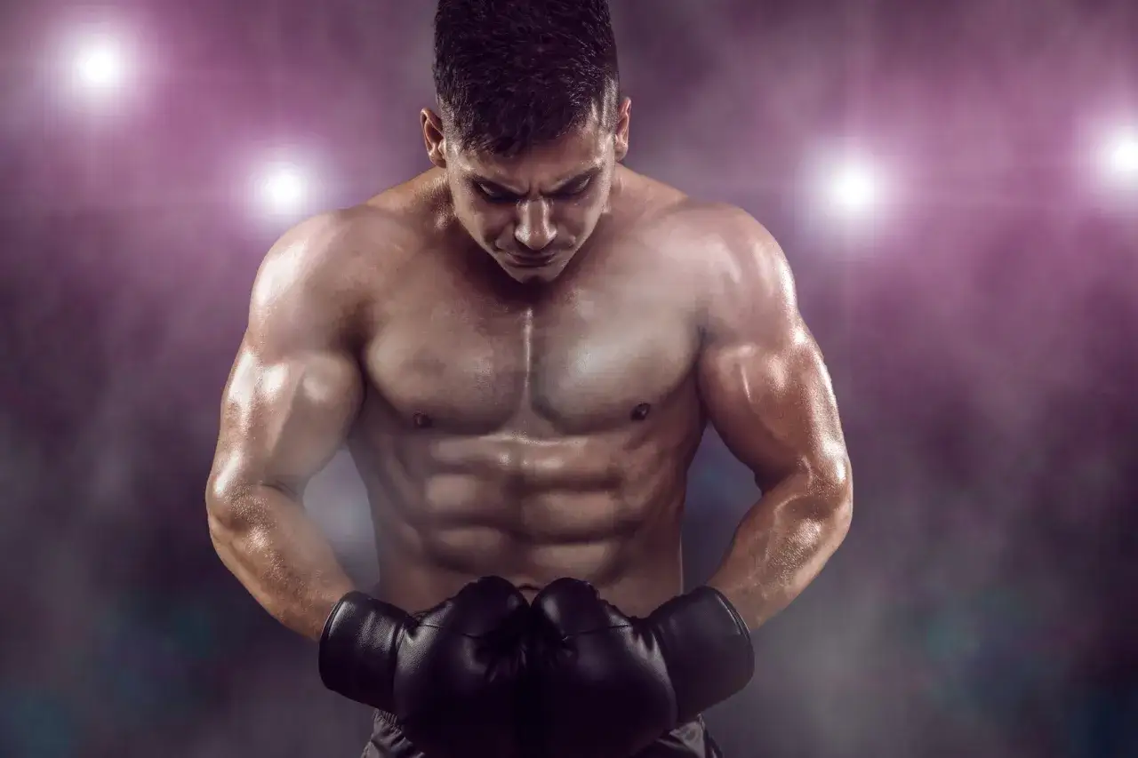 A muscular boxer with a defined boxing body, wearing black gloves, looks down intensely under stadium lights.