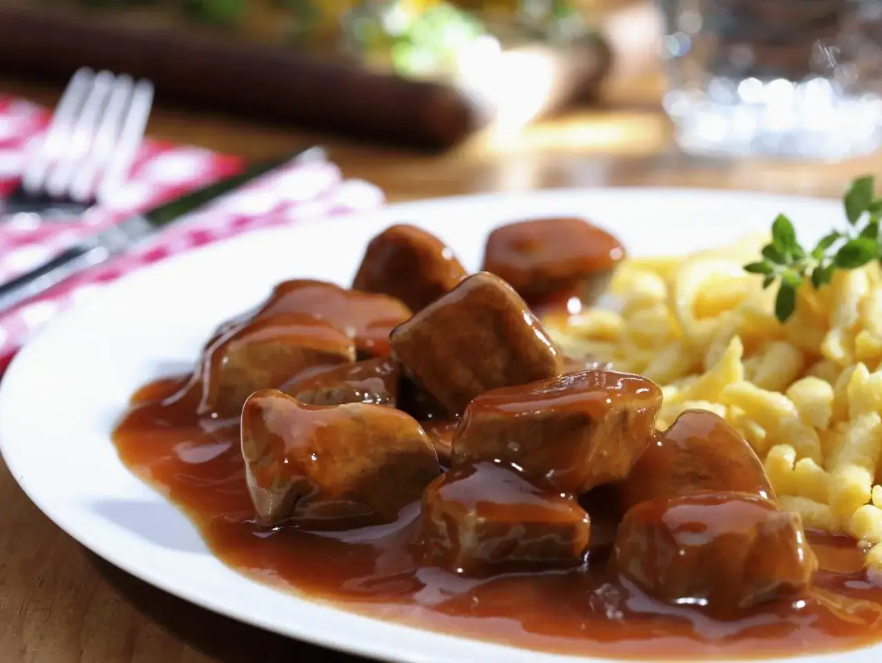Ein Teller mit saftigen Kalbfleischw&uuml;rfeln in dunkler Sauce und Sp&auml;tzle. Ein Festmahl, das nach dem besten Kalbsgulasch schmeckt.