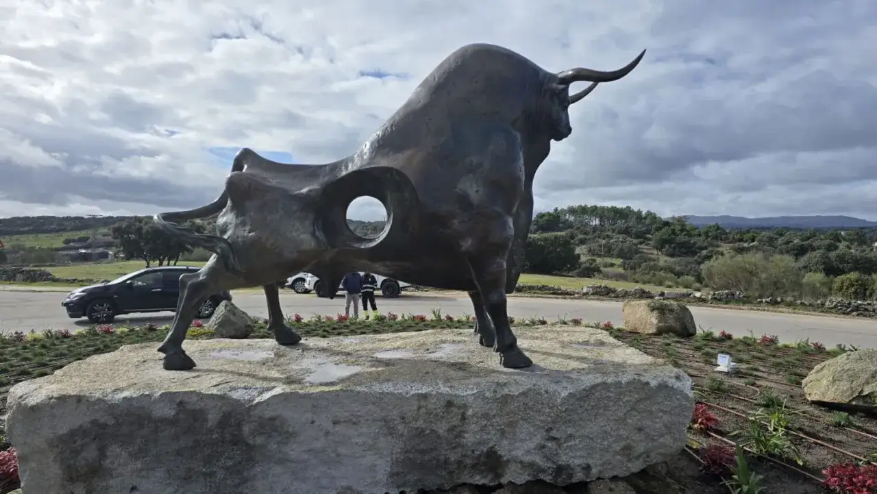Escultura de toro de bronce, s&iacute;mbolo de la plaza toros Valdemorillo, sobre una roca. Paisaje de monte y cielo nublado.
