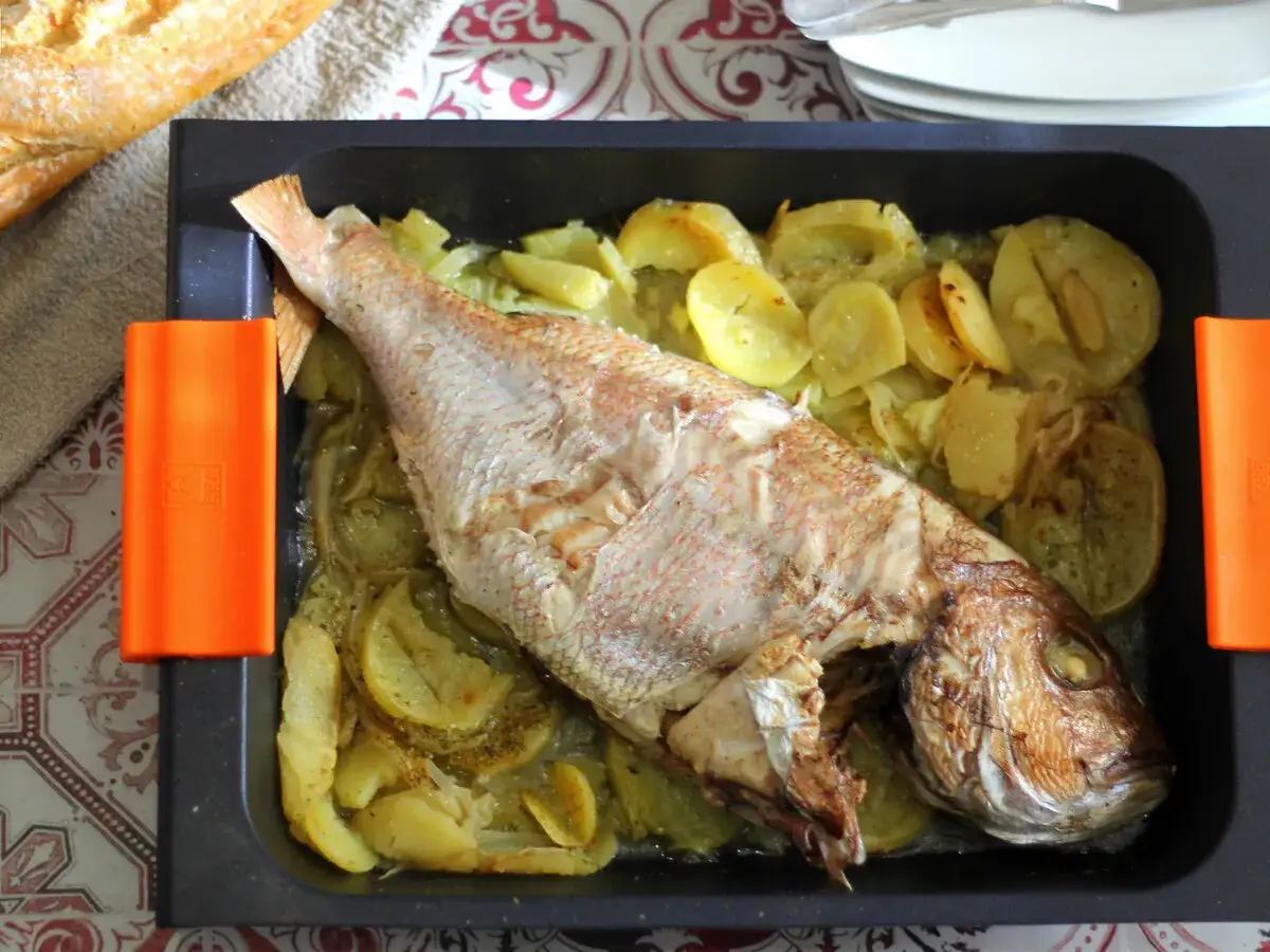 Pargo al horno con patatas y cebolla en una bandeja, listo para servir.